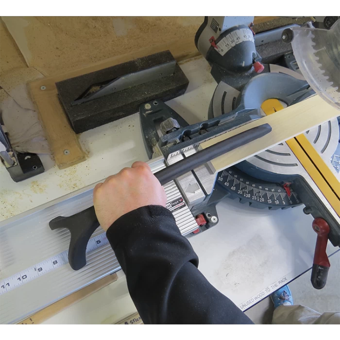 Woodworker using stick push block to guide wood safely on miter saw in workshop