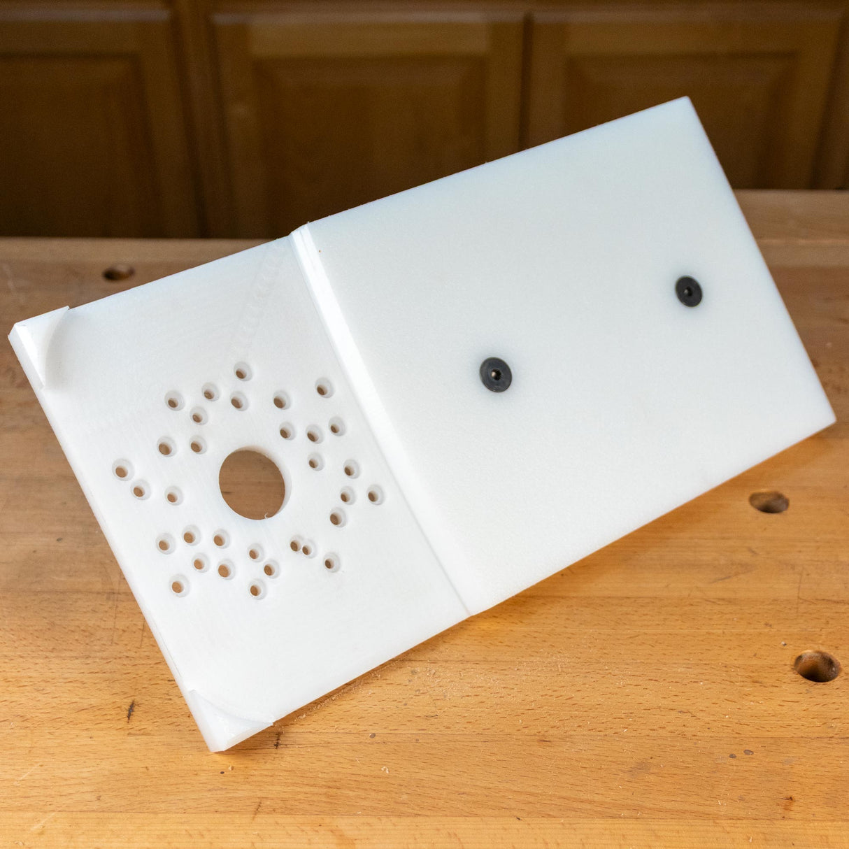 Woodworking router table insert plate with multiple mounting holes on a workbench