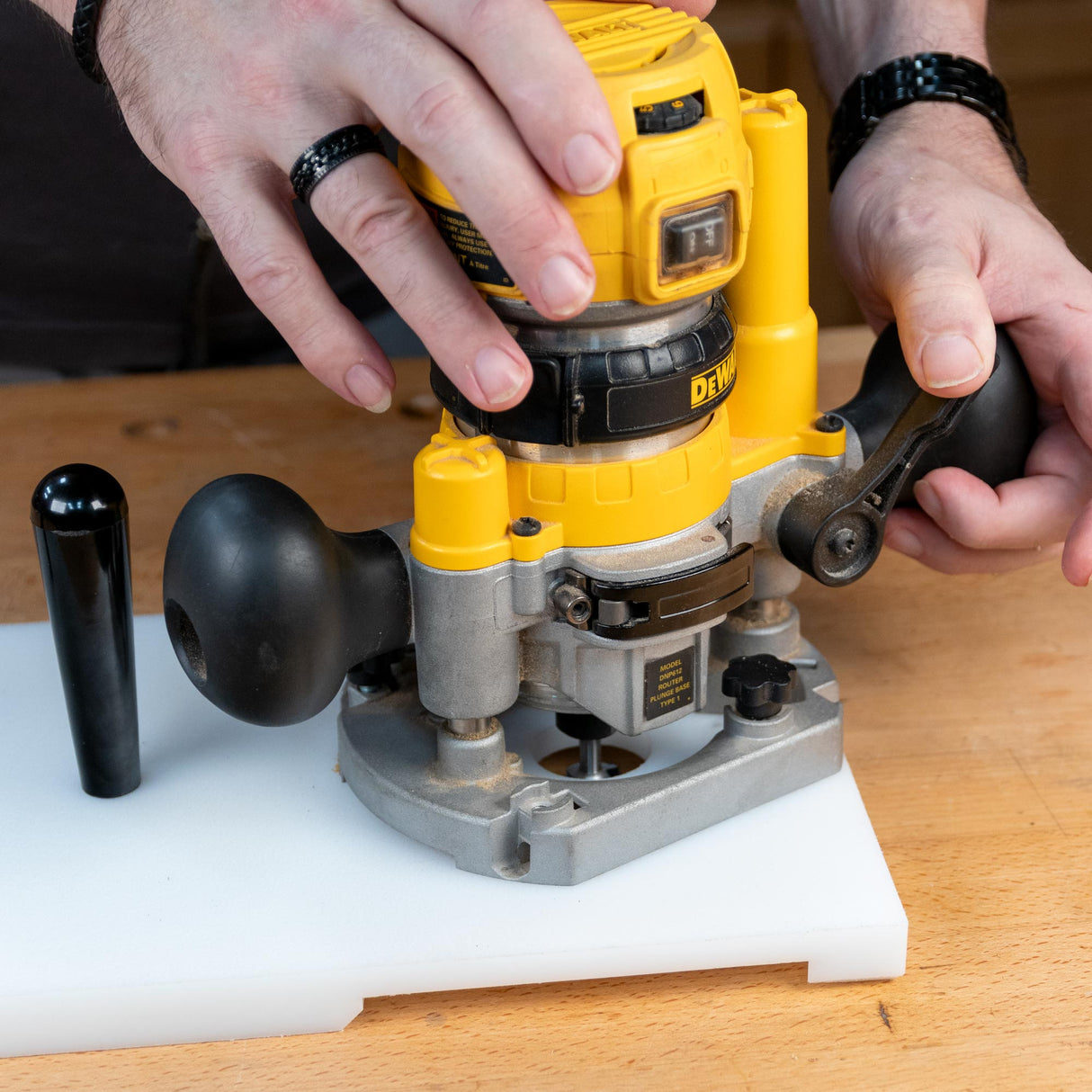 Hands operating a yellow woodworking router on a white work surface