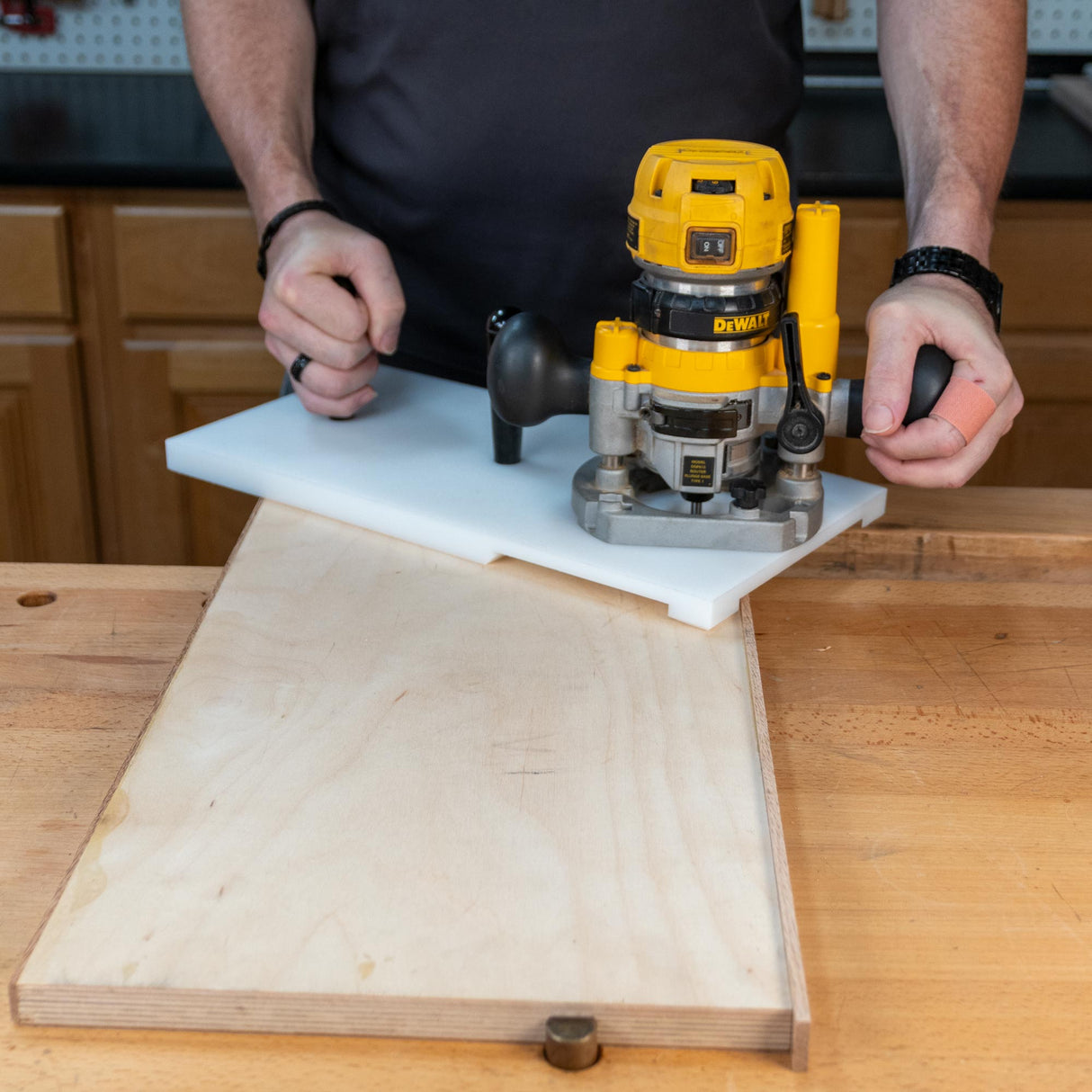 Woodworker using a router with guide to shape edge of plywood on workbench