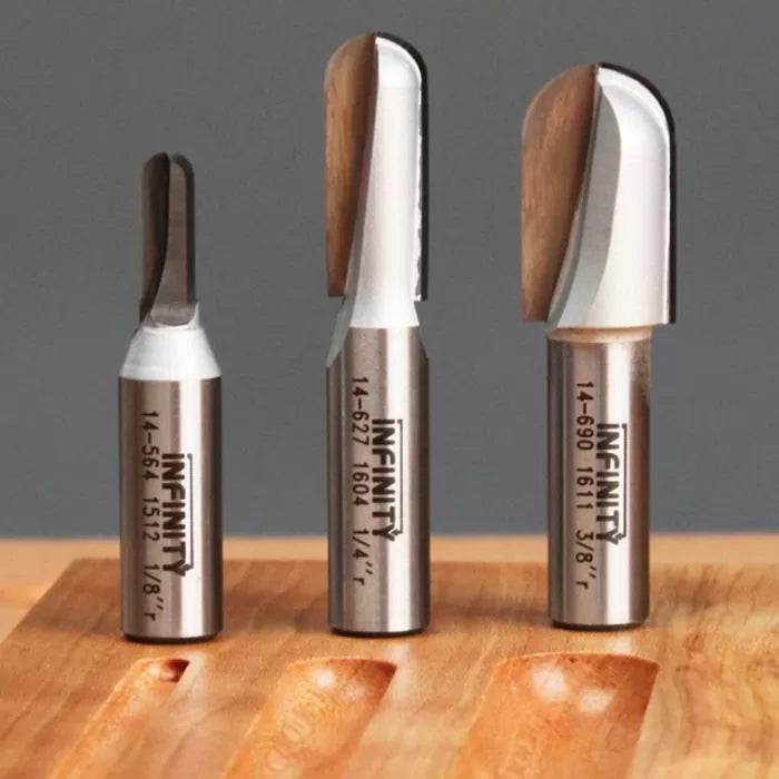 Three carbide router bits for woodworking displayed upright on a wooden surface.