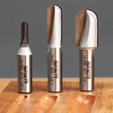 Three carbide router bits for woodworking displayed upright on a wooden surface.