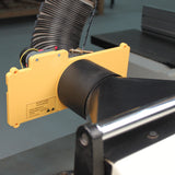 Woodworking dust collection hood with yellow safety guard attached to a machine table