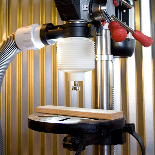 Drill press dust collection attachment with hose and clamp over wooden board