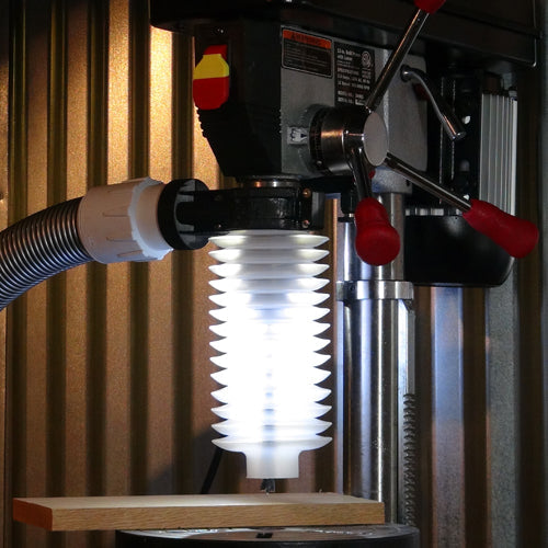 Drill press with dust collection hose and clear safety guard above a wooden board