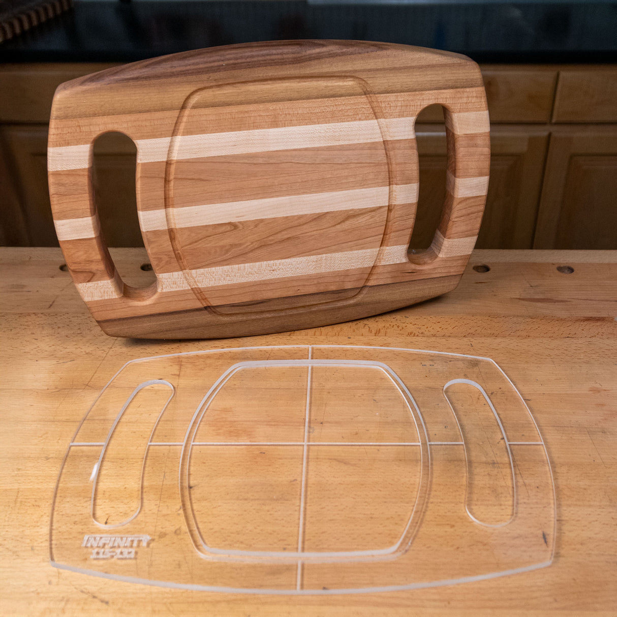 Clear acrylic cutting board template with cutout slots on wood workbench beside striped wooden cutting board