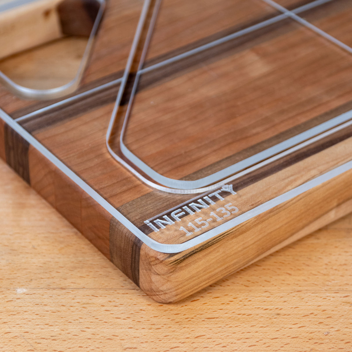 Acrylic cutting board template edge closeup on a wood surface, showing engraved markings.