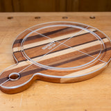 Acrylic cutting board template overlay on a round striped wooden cutting board on a workbench.