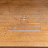 Clear acrylic handle template with etched guidelines on a wooden workbench.