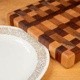 Wooden cutting board with checkered pattern and floral rim plate on wood surface