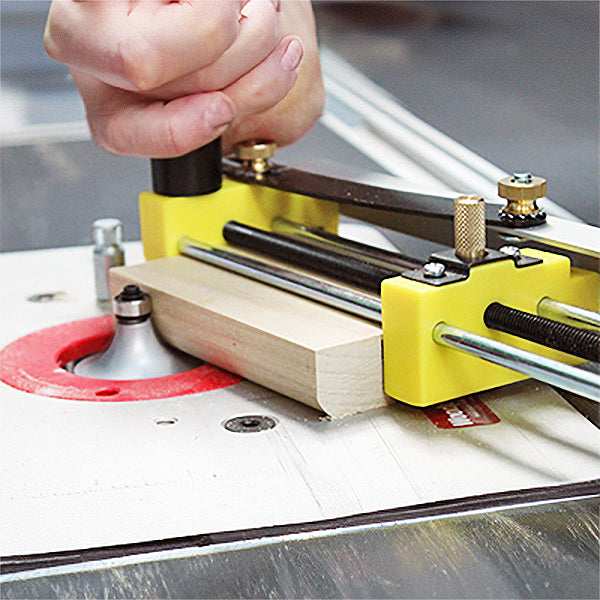 Woodworker using yellow router table jig to guide wood block with router bit for precise cuts