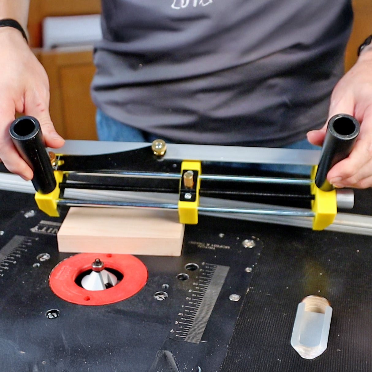 Woodworker using router table jig with yellow and black handles to guide wood block