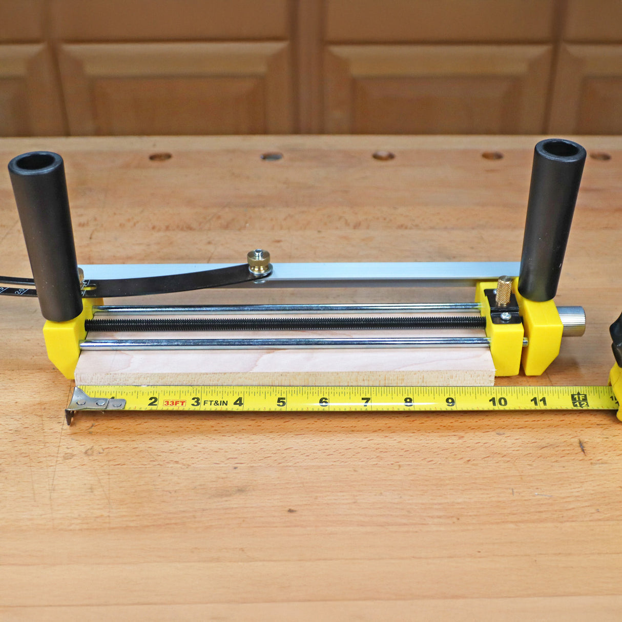 Woodworking edge guide tool with yellow clamps and measuring tape on workbench