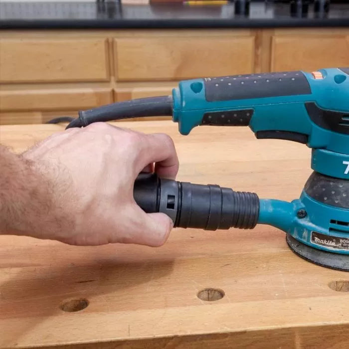 Hand connecting dust collection hose to orbital sander on woodworking bench
