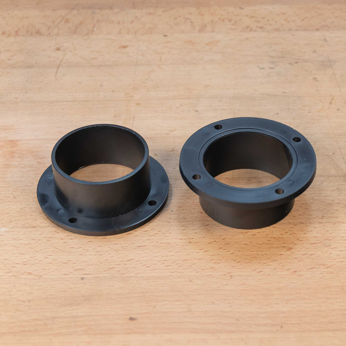 Two black plastic 2-1/2 inch dust connectors with mounting flanges on a wooden workbench.