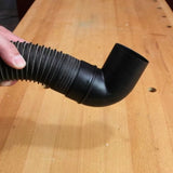 Hand holding a flexible dust collection hose with a black elbow fitting on a woodworking bench