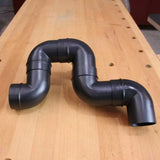Black plastic dust collection fittings with multiple elbows on a woodworking bench