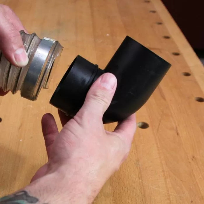 Hands connecting dust collection hose to black plastic elbow fitting on workbench