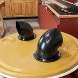 Black plastic dust collection ports mounted on a yellow drum lid in a woodworking shop
