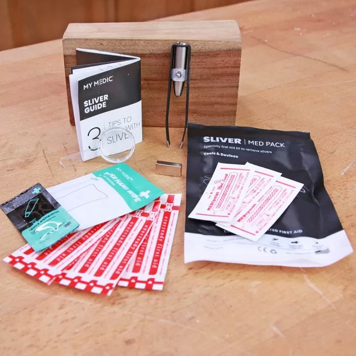 Woodworking sliver removal first aid kit with guide, tweezers, bandages, and packaging on workbench