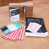 Woodworking sliver removal first aid kit with guide, tweezers, bandages, and packaging on workbench