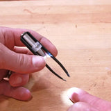 LED lighted tweezers held over a wooden workbench, hand reaching to use the tool