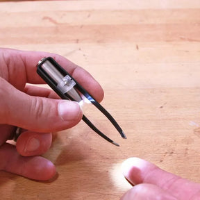LED lighted tweezers held over a wooden workbench, hand reaching to use the tool