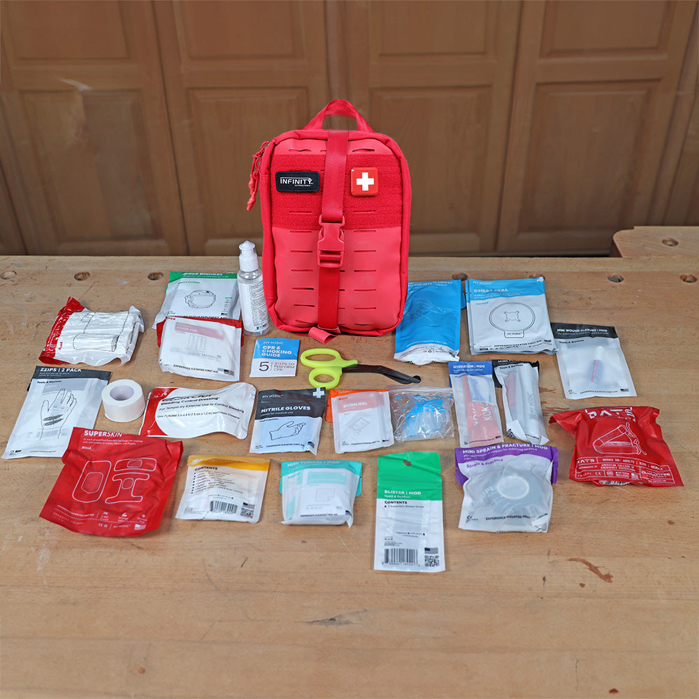Red first aid kit with medical supplies and tools organized on a wooden workbench.