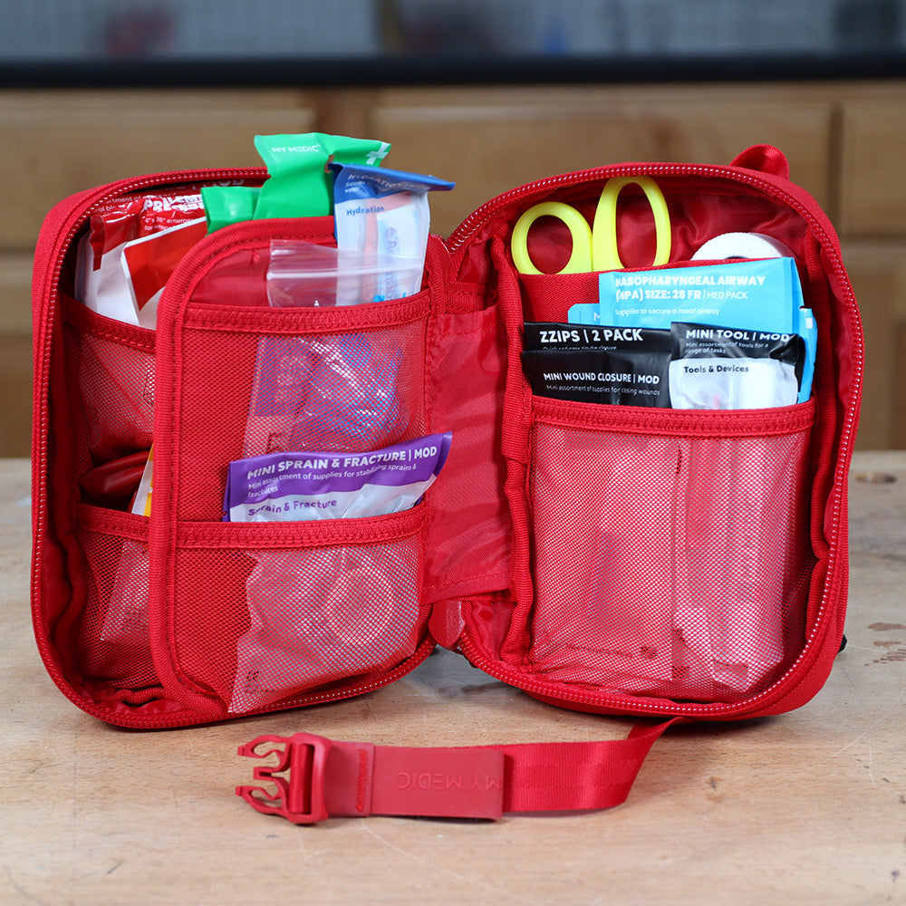 Red first aid kit open on workbench, showing medical supplies and emergency tools organized in mesh pockets.