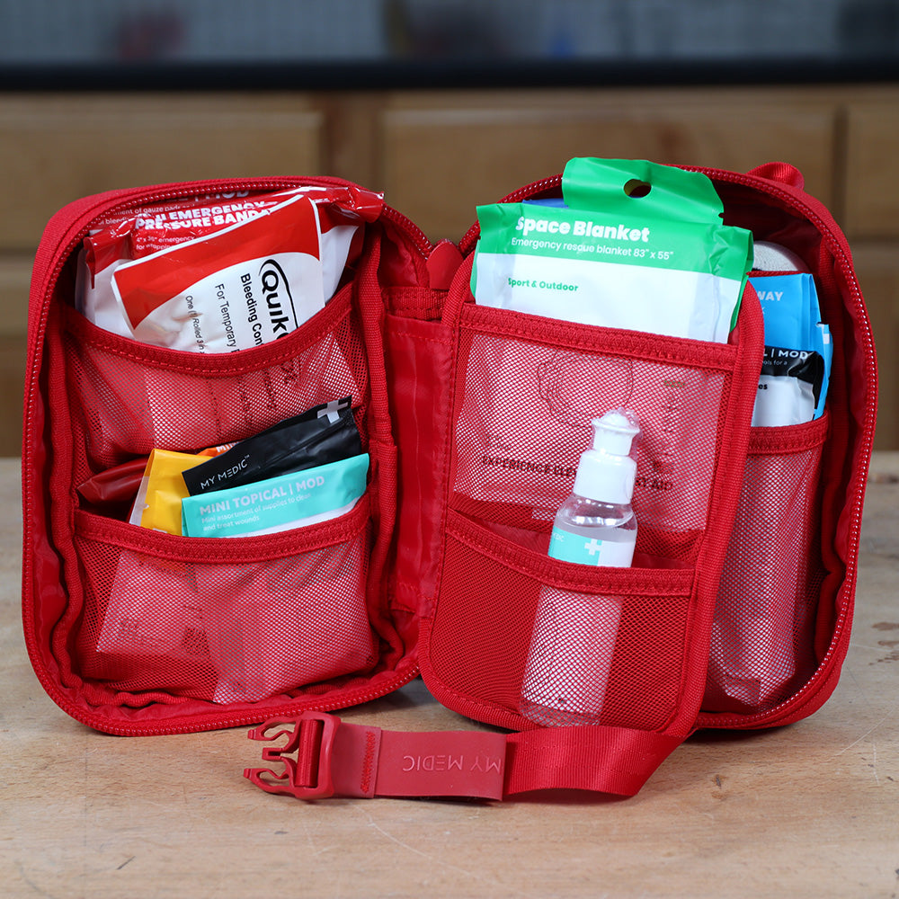 Open red first aid kit with emergency bandages, topical wipes, space blanket, and sanitizer