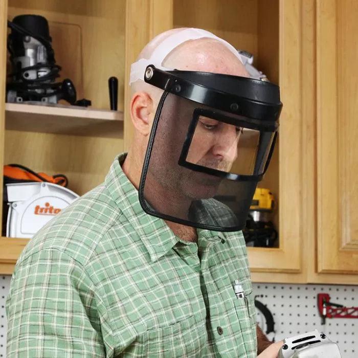 Man in workshop wearing safety face shield, using woodworking tool, protective gear focus