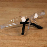 Clear safety glasses with black temples on a wooden surface, ideal for woodworking protection.