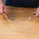 Clear safety glasses with black arms held over a woodworking bench for eye protection