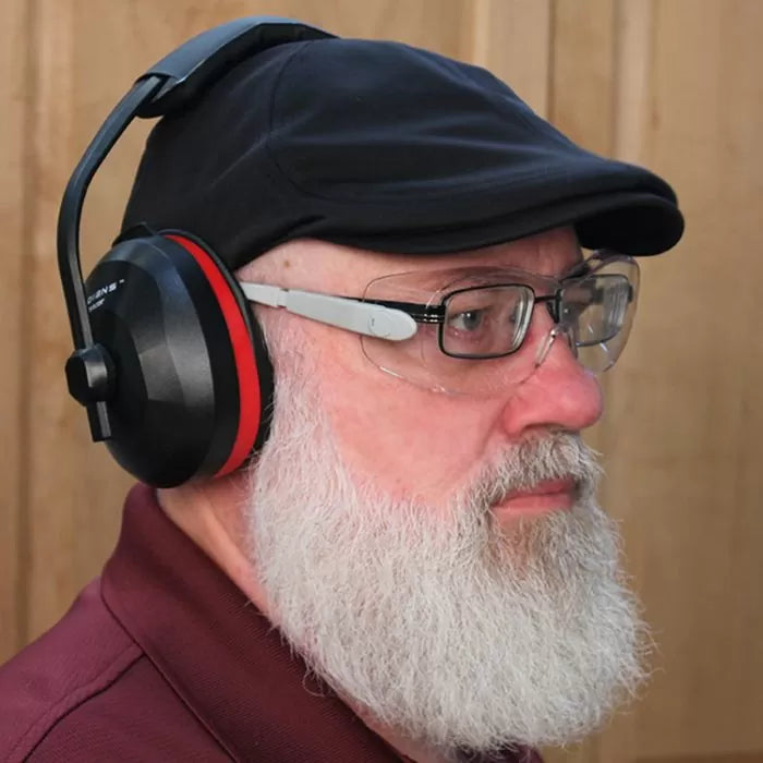 Man wearing safety glasses, ear protection, and a black cap in a woodworking shop