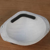 White dust mask with foam nose pad on a wood surface, woodworking safety gear
