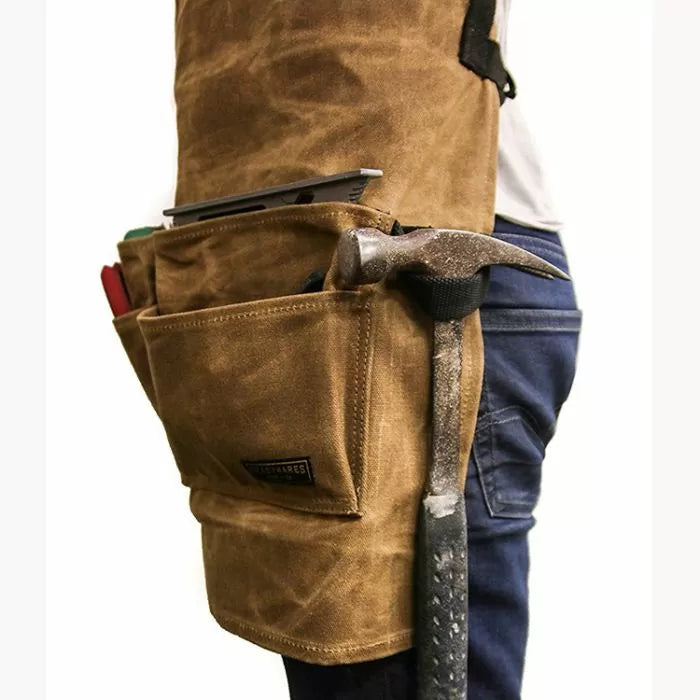 Brown waxed canvas woodworking tool apron with pockets holding hammer and hand tools
