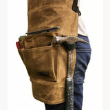 Brown waxed canvas woodworking tool apron with pockets holding hammer and hand tools