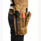 Brown canvas woodworking tool apron with pockets holding hand tools, worn at the waist