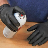 Person wearing black gloves holding adhesive spray can on woodworking table
