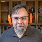 Man wearing orange NRR 24 earmuffs and safety glasses in a woodworking shop