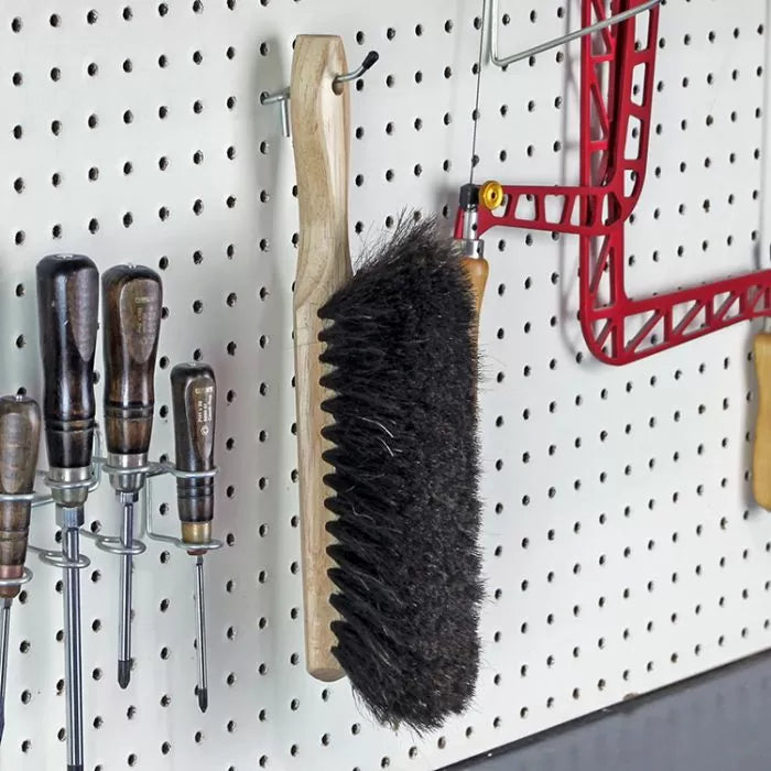 Wood handle bench brush hanging on pegboard with screwdrivers and woodworking tools