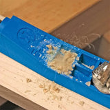 Blue woodworking pocket hole jig clamped to wood with drill and wood shavings visible