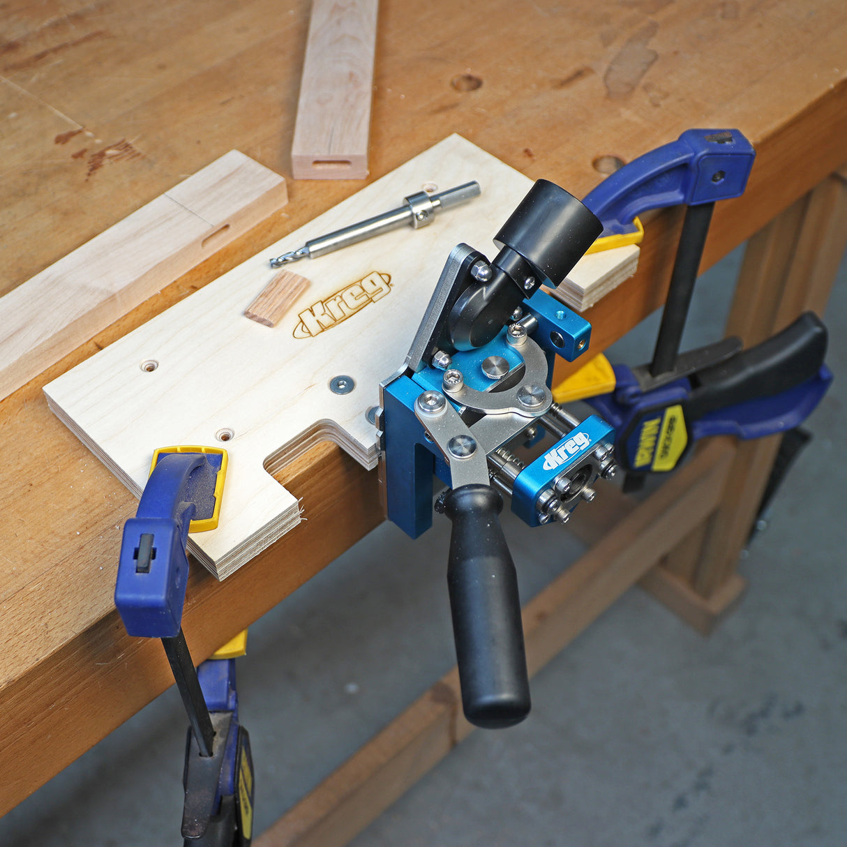 Woodworking mortise jig clamped to workbench with handle, drill bit, and wood pieces