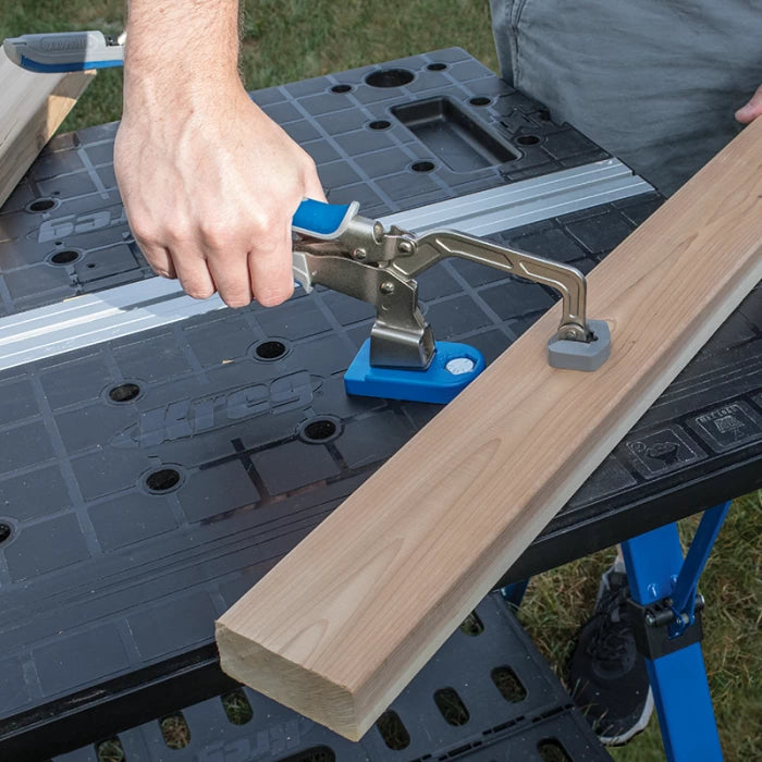 Hand using woodworking clamp to secure board on portable workbench outdoors