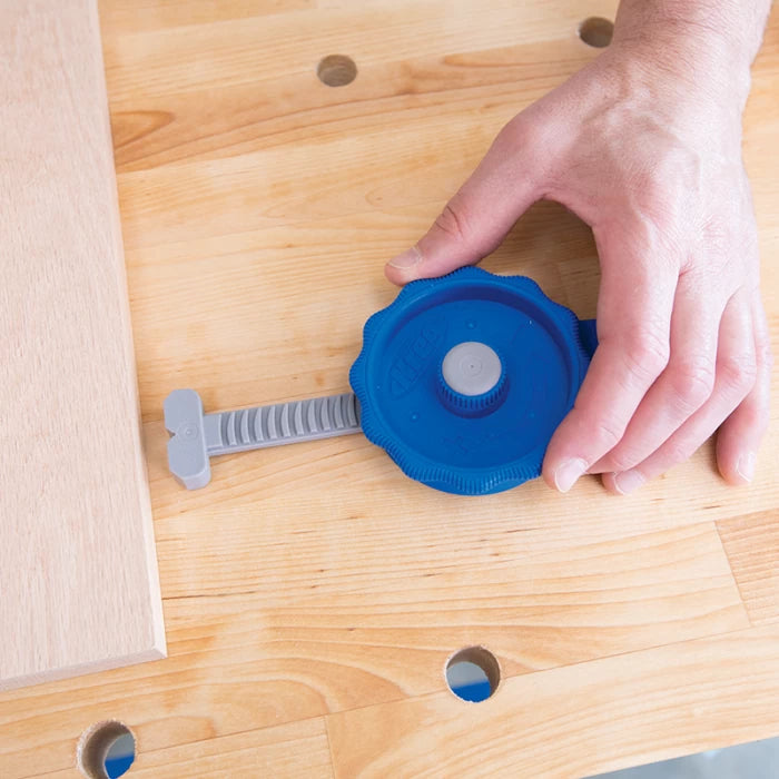 Hand adjusting blue workbench clamp on wooden table for woodworking project