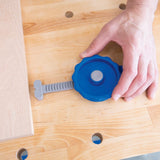 Hand adjusting blue workbench clamp on wooden table for woodworking project