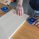 Woodworker securing a wooden board on a workbench with blue woodworking clamps
