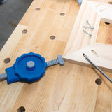 Woodworking clamp holding mitered wood pieces on workbench with screws and screwdriver
