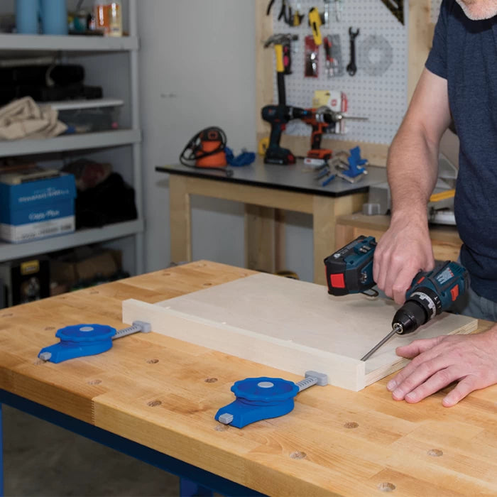 Woodworker using cordless drill on clamped board at workbench in woodworking shop
