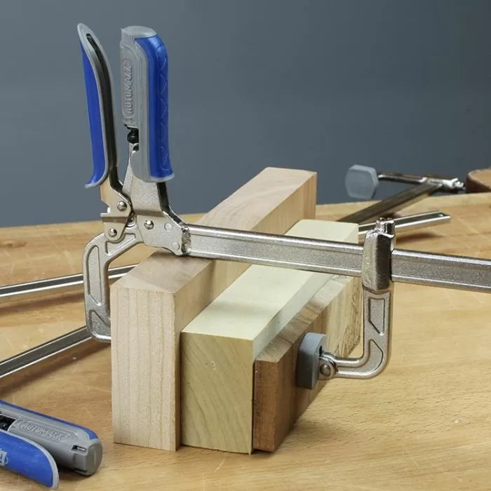 Woodworking clamp with blue handle securing wood blocks on a workbench